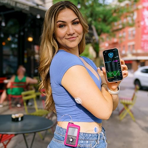 Woman holding phone wearing the MiniMed 780G pump and Simplera Sync sensor on her arm